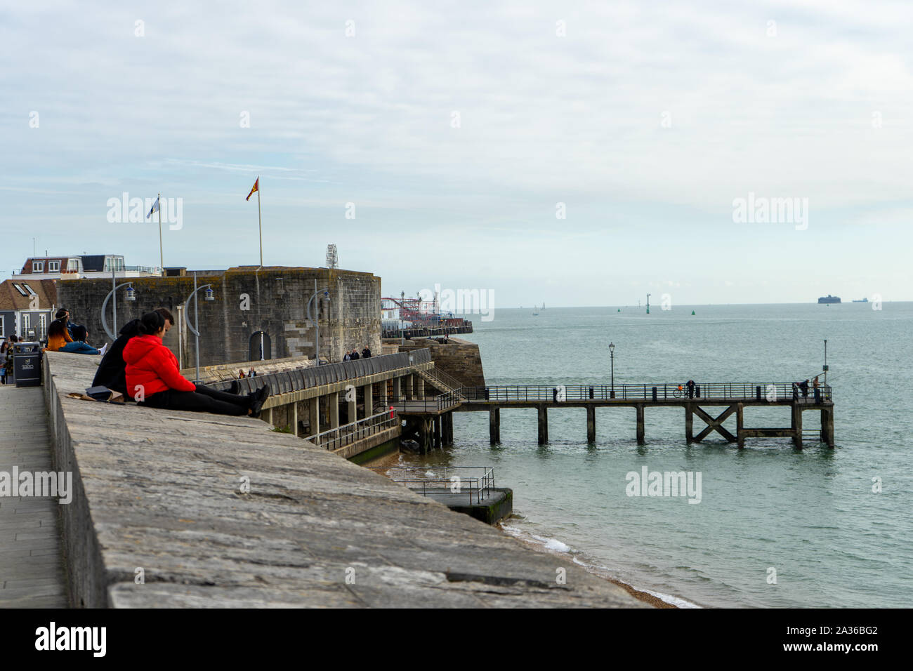 A couple sat talking sitting on the walls at Old Portsmouth looking out to sea Stock Photo