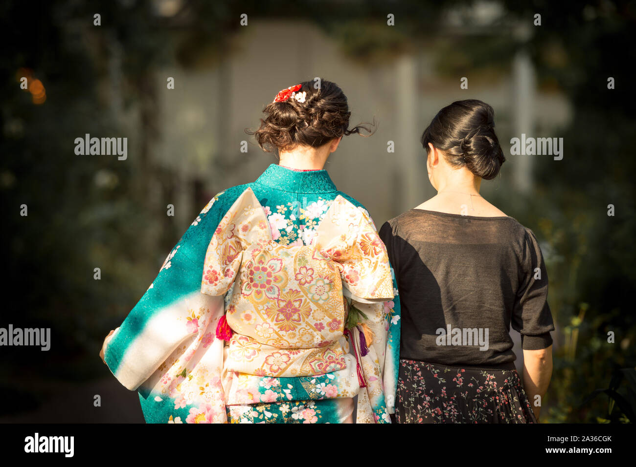 A Japanese woman wearing kimono accompanied by another woman in black dress. Stock Photo