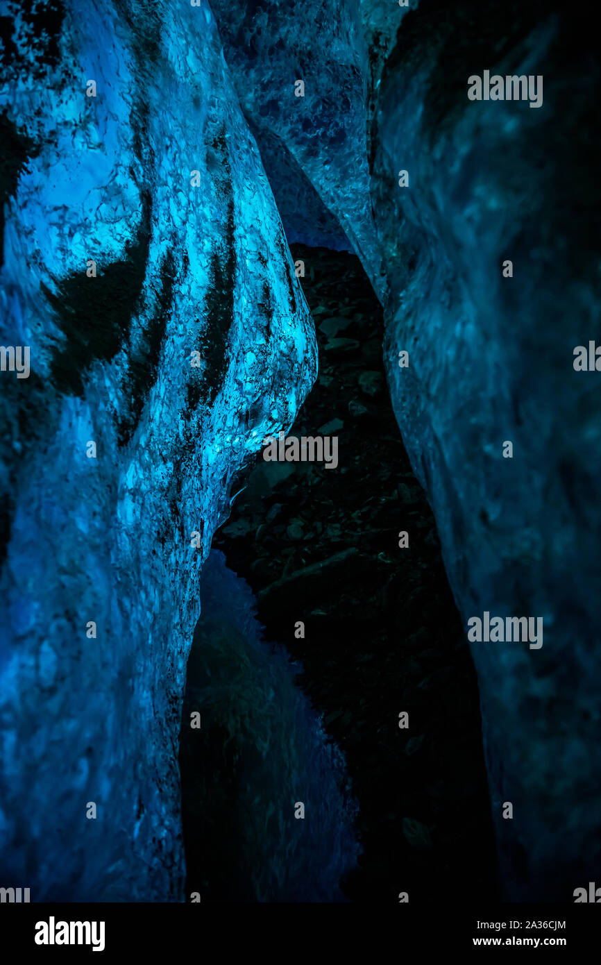 Light from above the Salmon Glacier shining down through the blue ice below into this deep, dark ice cave. Rocks brought in by the river line the floo Stock Photo