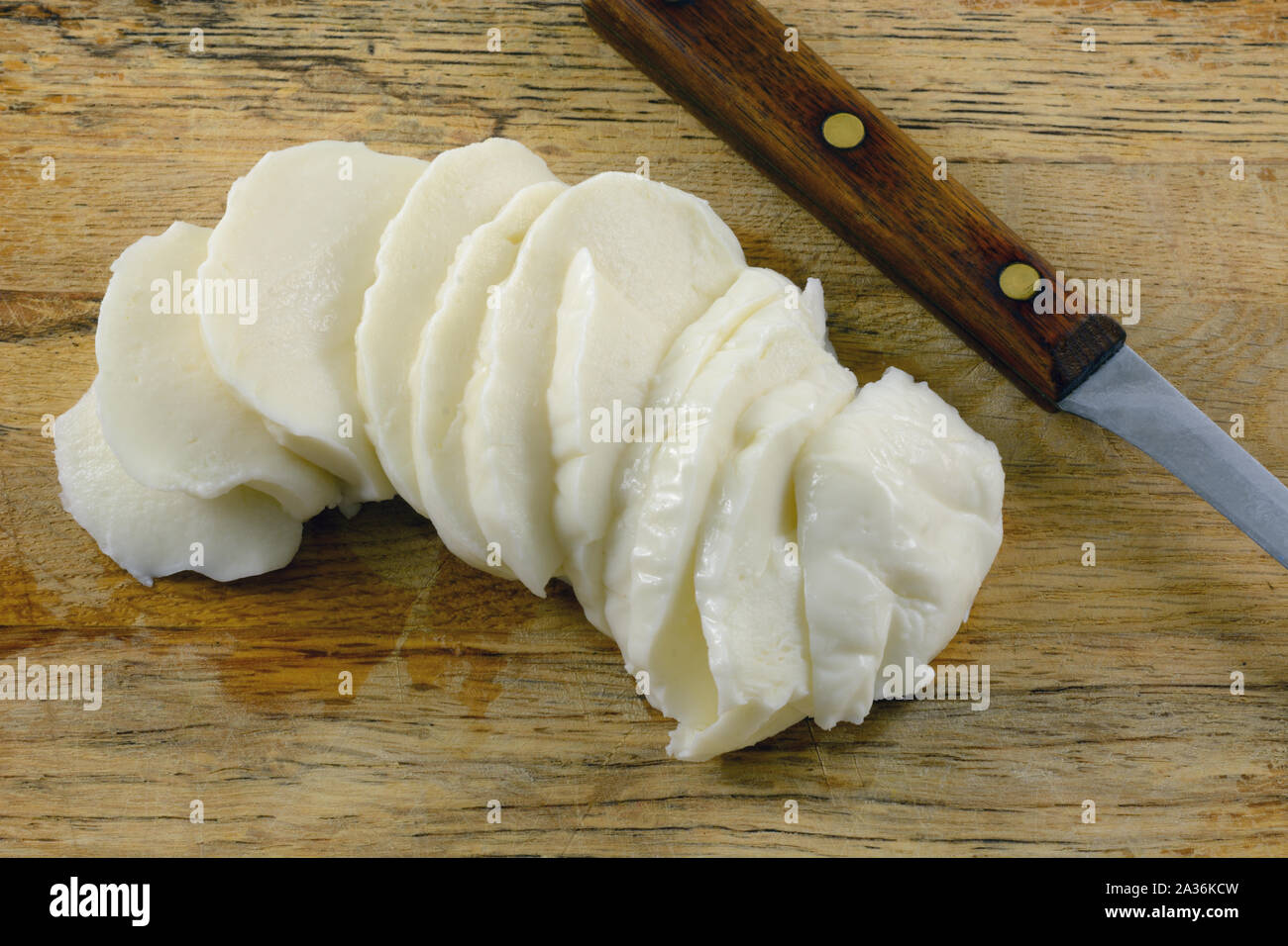 Fresh mozzarella cheese slices on wooden cutting board with kitchen knife Stock Photo