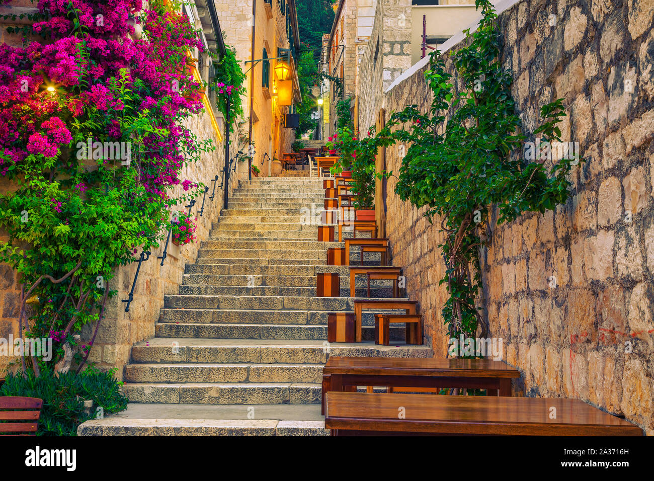 Cozy narrow street with street cafe and restaurant at morning. Rustic street with stone houses and colorful bougainvillea mediterranean flowers, Hvar Stock Photo