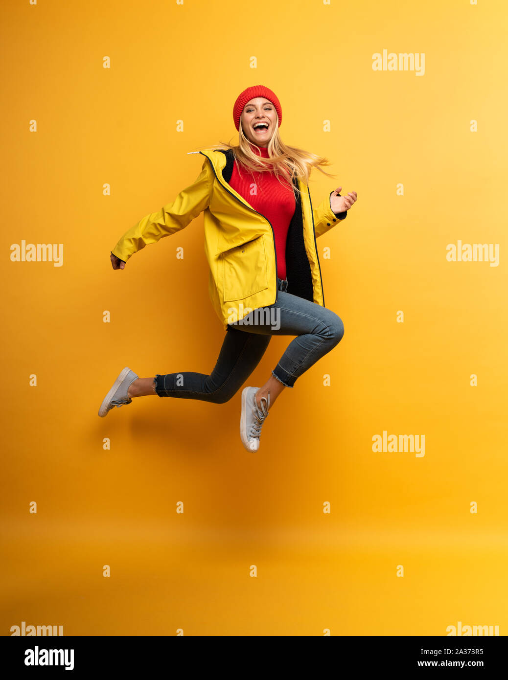 Girl with jacket jumps to the sun from the rainy weather. Joyful expression. Yellow background Stock Photo