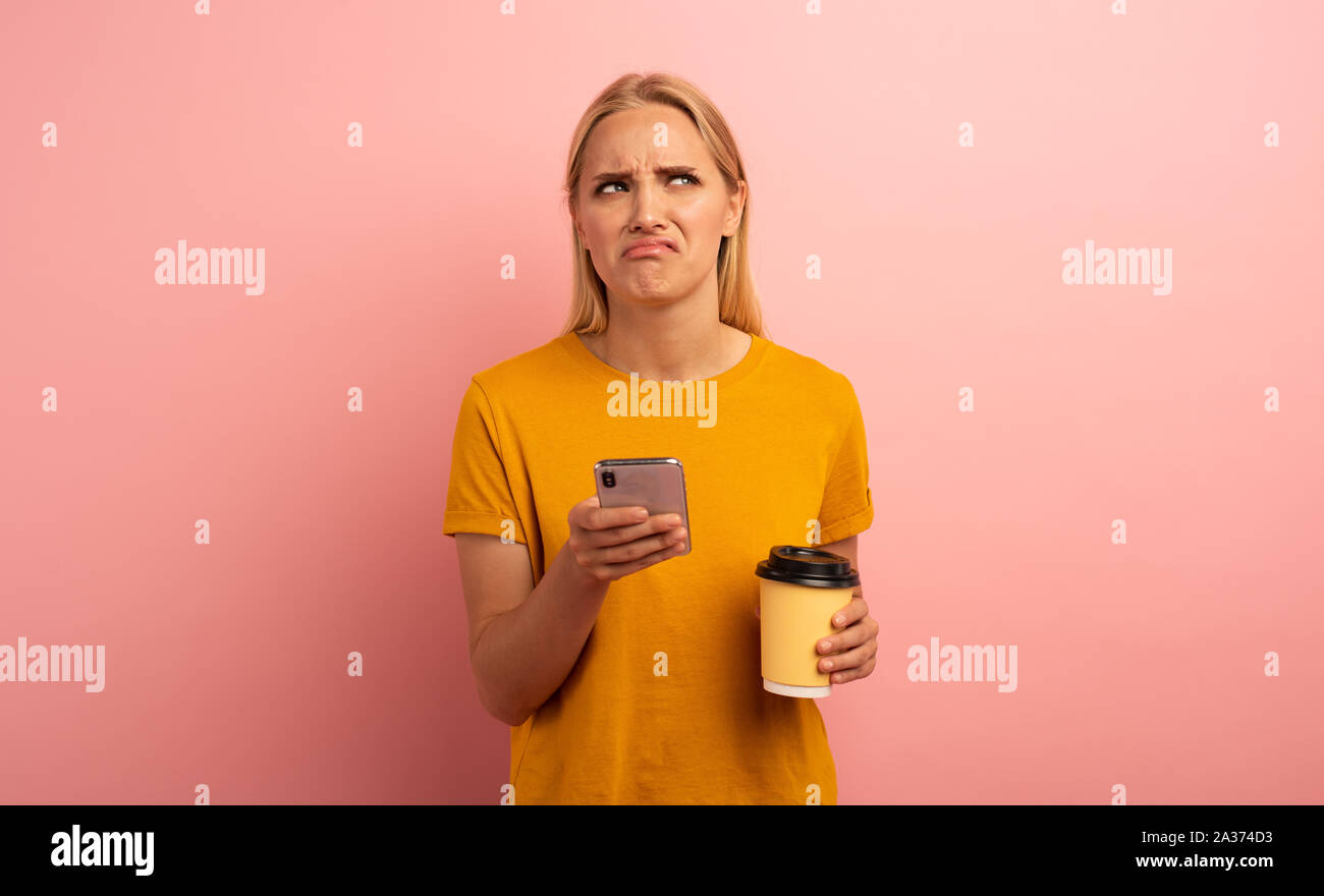 Blonde girl thinks about the right option. Yes or no. Confused and pensive expression. Pink background Stock Photo