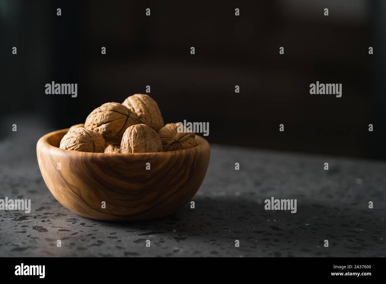 inshell walnuts in olive wood bowl on terrazzo countertop, shallow focus Stock Photo
