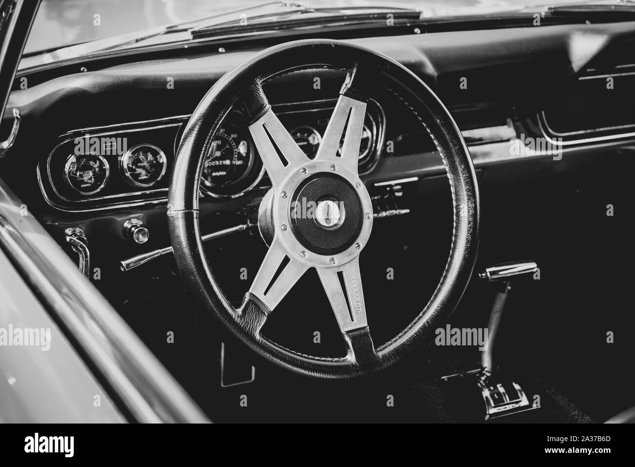 A black and white portrait of the steering wheel, dashboard and clutch