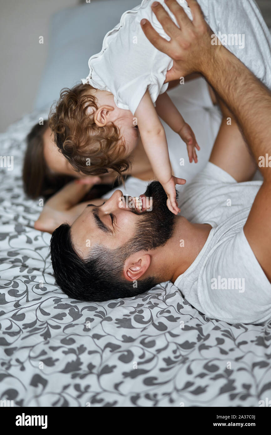 happy young family playing with their baby while laying on the bed at home, holding kid above their heads . close up side view photo Stock Photo