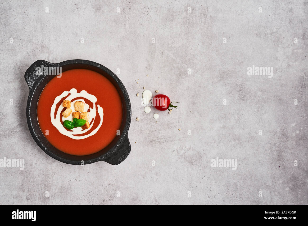 Tomato soup with cream, croutons and basil in a black bowl on stone background. Top view. Copy space for text. Stock Photo