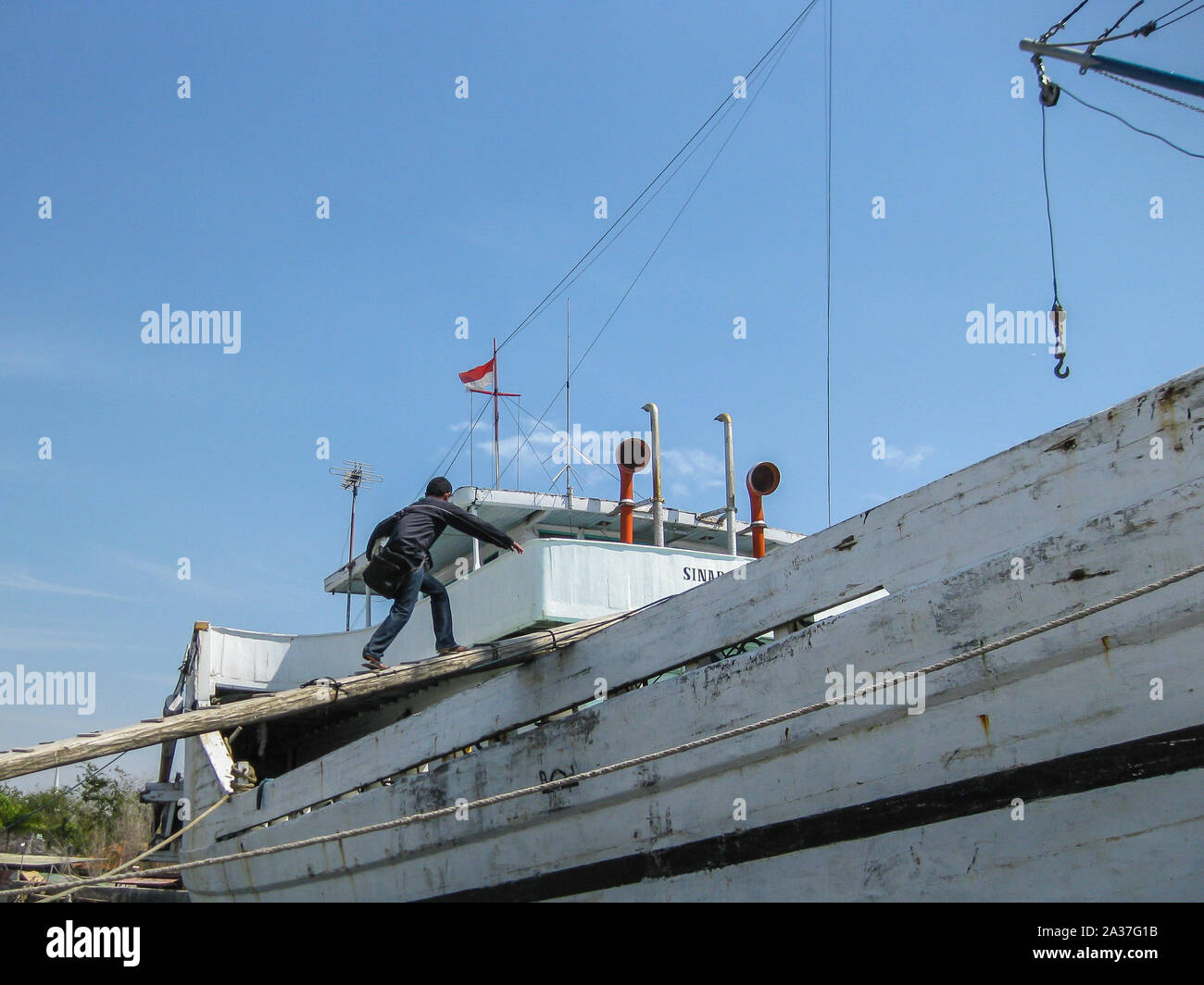 Jakarta, Indonesia - July 13, 2009: a man ascends a wooden ship on a wooden beam in front of a wooden ship in white, green and red Stock Photo
