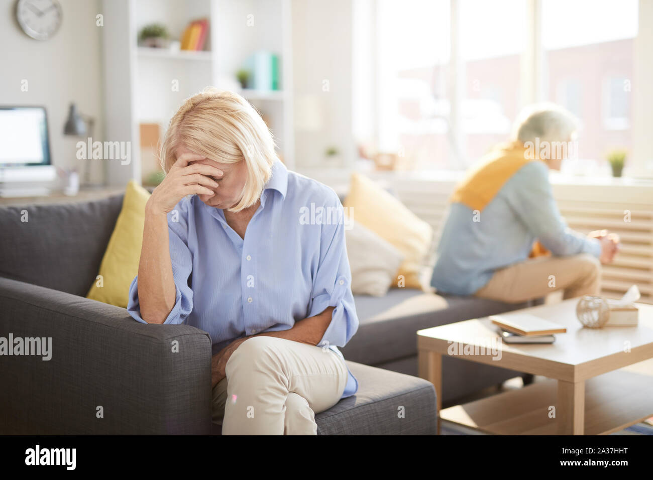 Portrait of senior couple fighting sitting on opposite sides of sofa at home, focus on frustrated wife in foreground, copy space Stock Photo