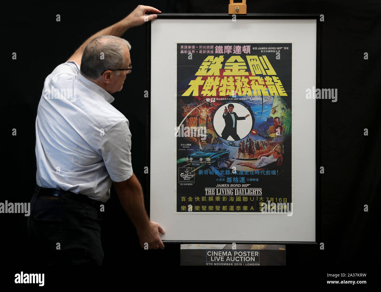 Store poster consultant Mike Bloomfield adjusts a Carlsberg Poster for the 1987 James Bond film The Living Daylights (estimate Â£100-200) during a preview for the Prop Store's forthcoming cinema poster live auction. PA Photo. Picture date: Thursday September 19, 2019 Photo credit should read: Andrew Matthews/PA Wire Stock Photo