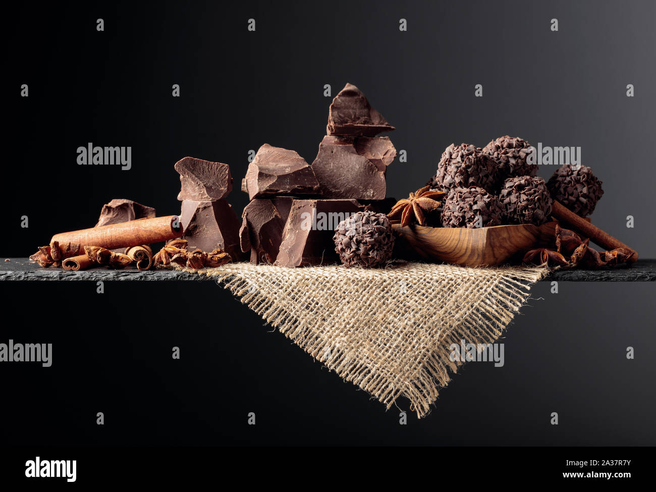 Chocolate truffles with broken pieces of chocolate and spices. Chocolate, cinnamon sticks and anise on a dark background. Copy space. Stock Photo
