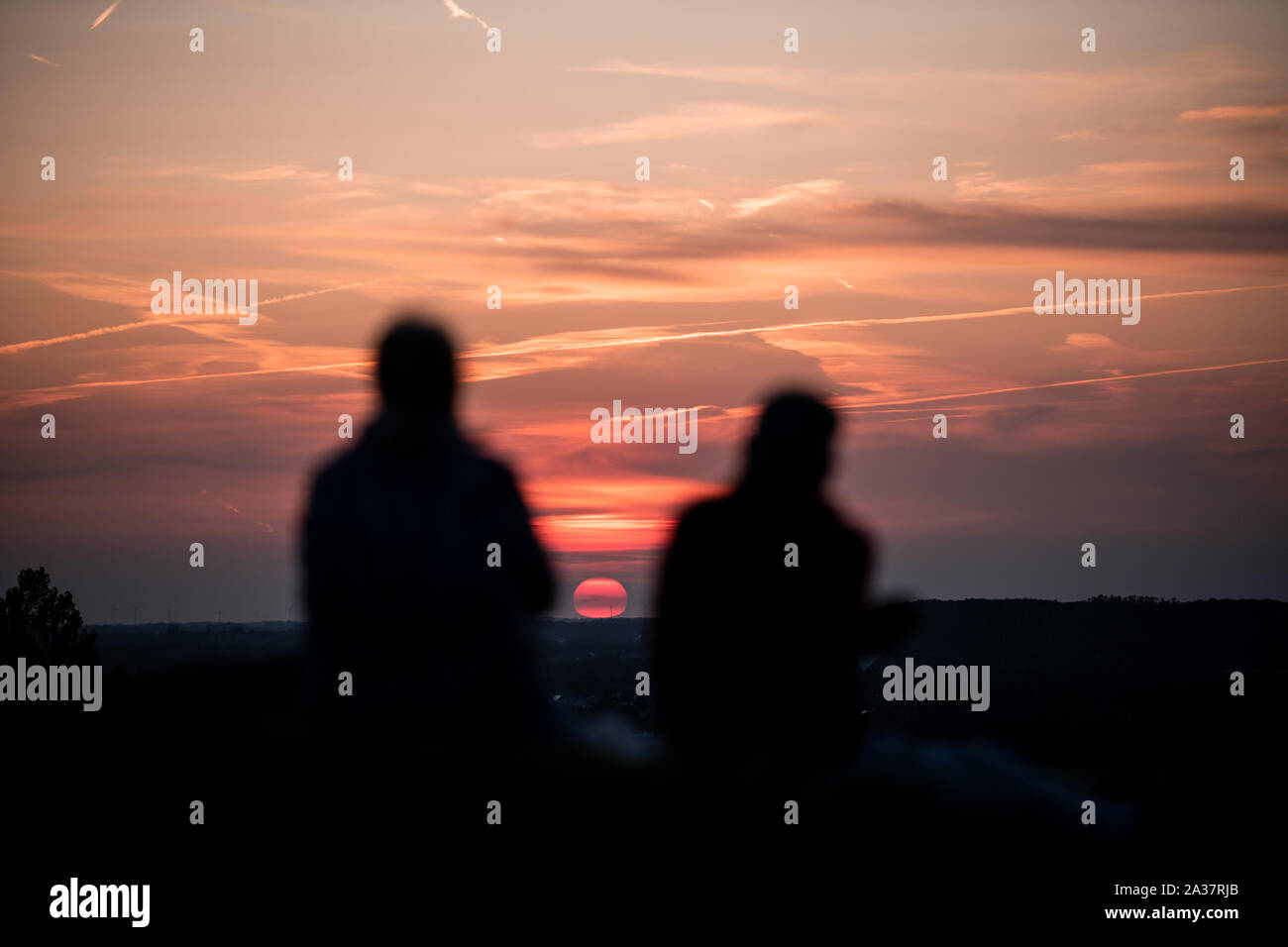Silhouetten von Personen vor dem Himmel mit untergehender Sonne auf der Halde Rheinpreussen in Moers. Stock Photo
