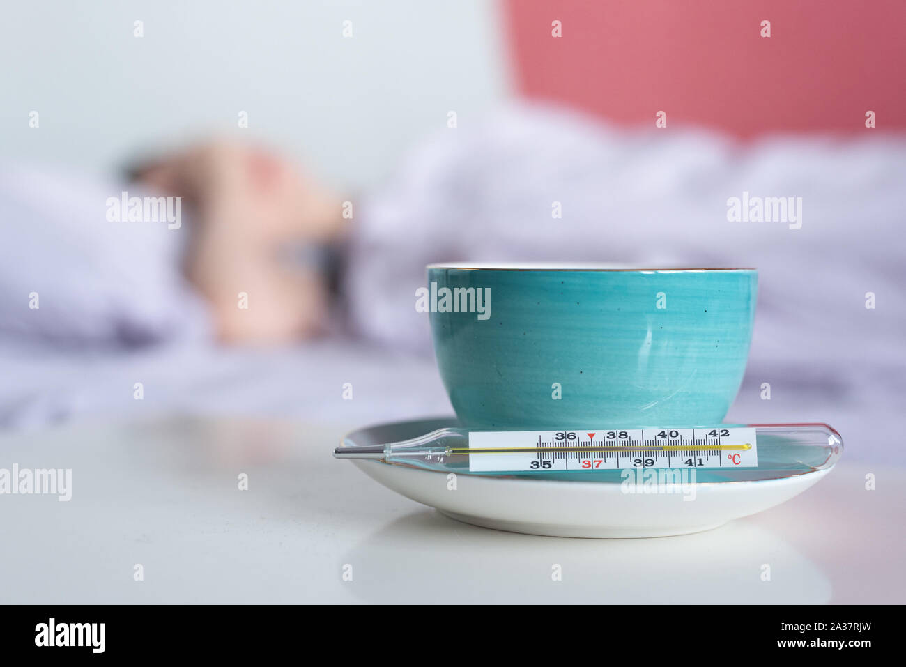 A cup of tea, thermometer with high body temperature and flu sick woman in bed background. Stock Photo
