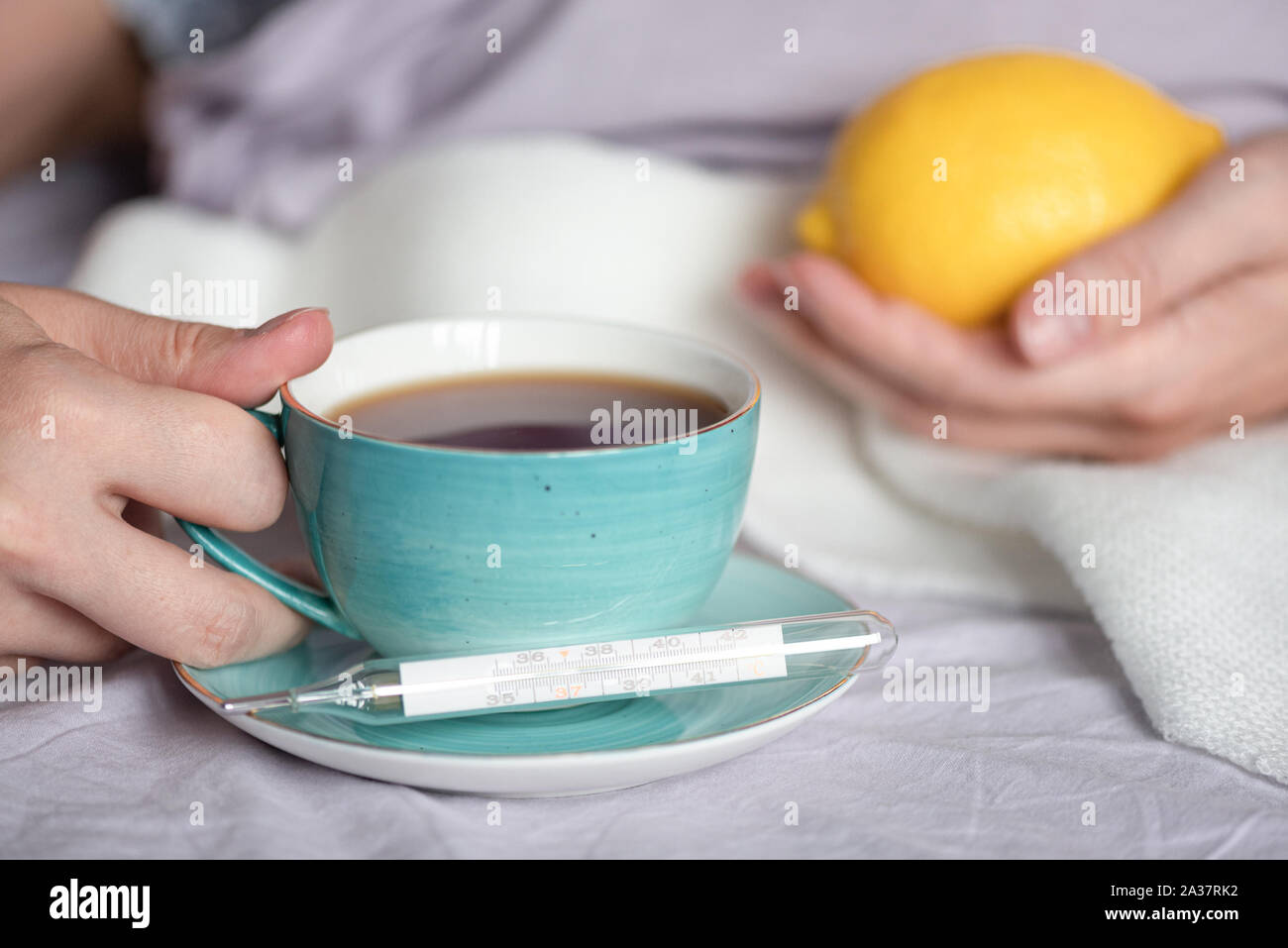 Cup of tea with fresh lemon and a thermometer with high body temperature. Stock Photo