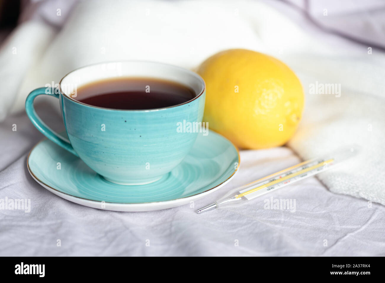 Cup of tea with fresh lemon and a thermometer with high body temperature. Stock Photo