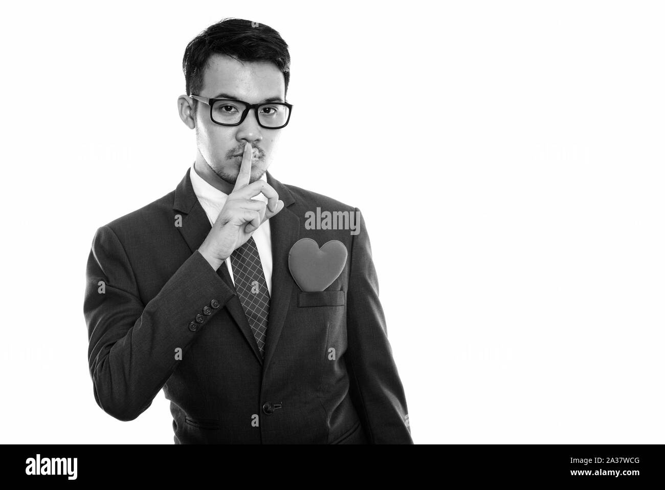 Studio shot of young Asian businessman with finger on lips and red heart on chest Stock Photo