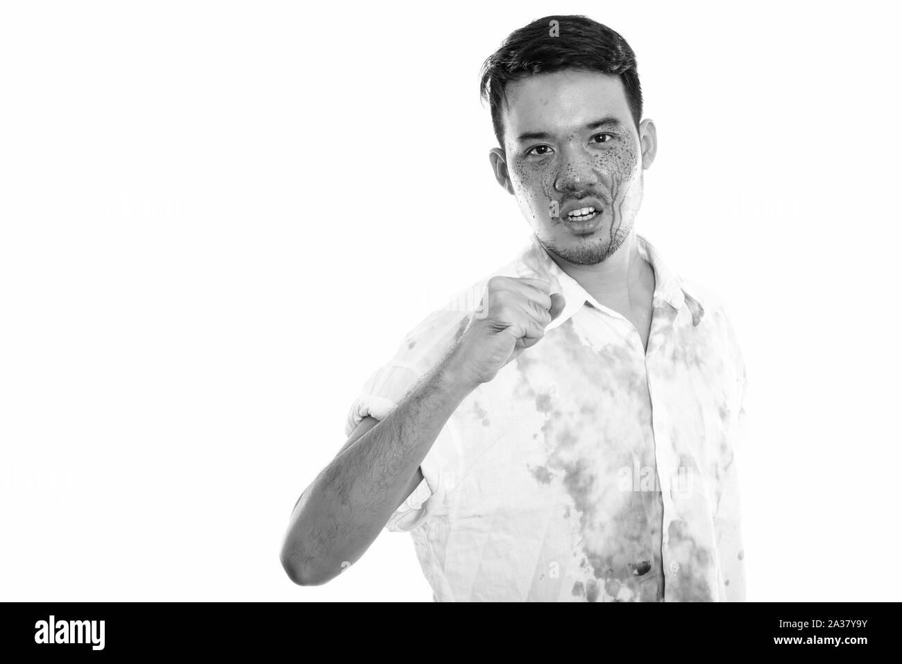 Studio shot of young crazy Asian man with fist raised with blood on face Stock Photo