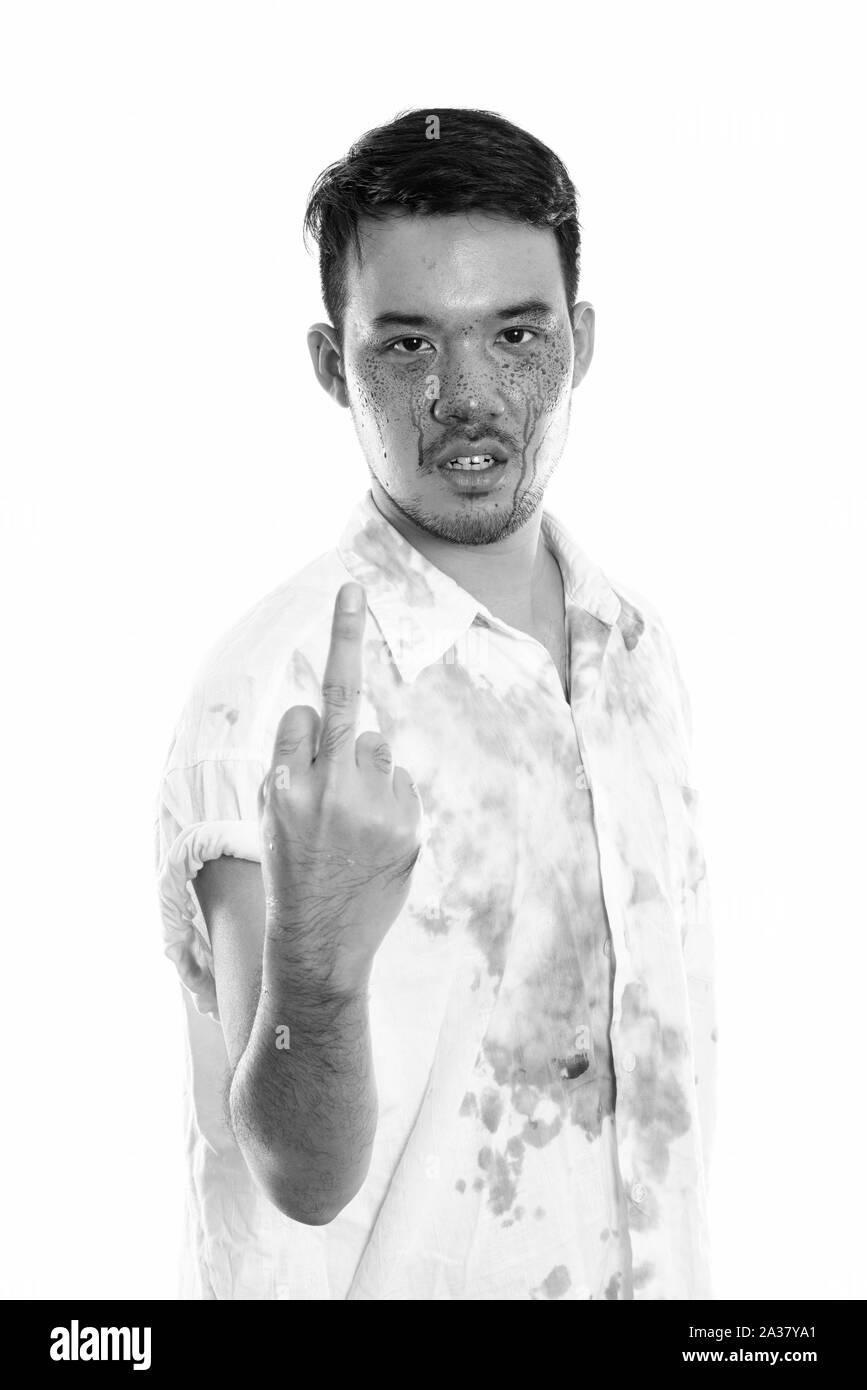 Studio shot of young crazy Asian man showing his middle finger with blood on face Stock Photo