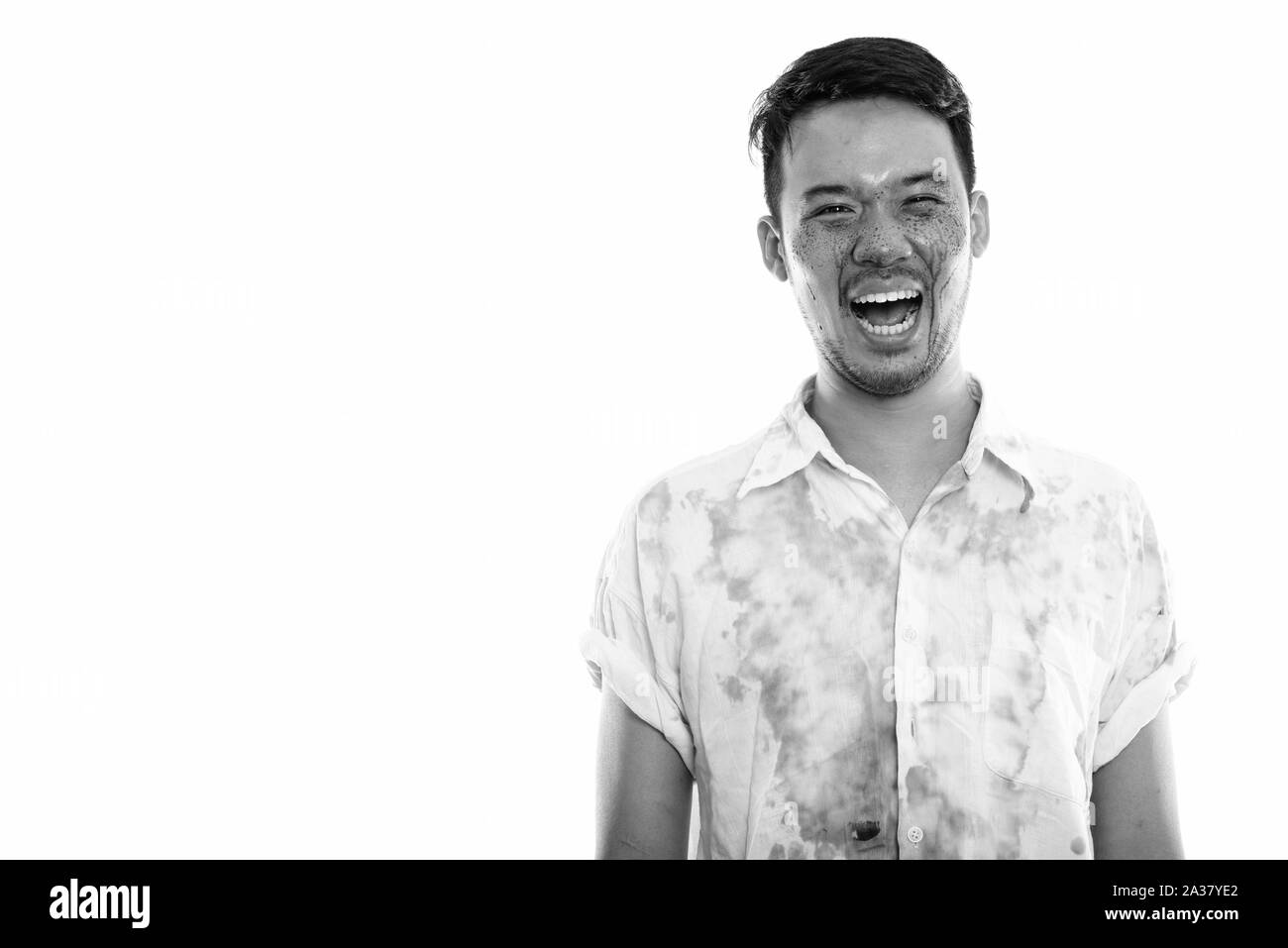 Studio shot of young happy crazy Asian man smiling and laughing with blood on face Stock Photo