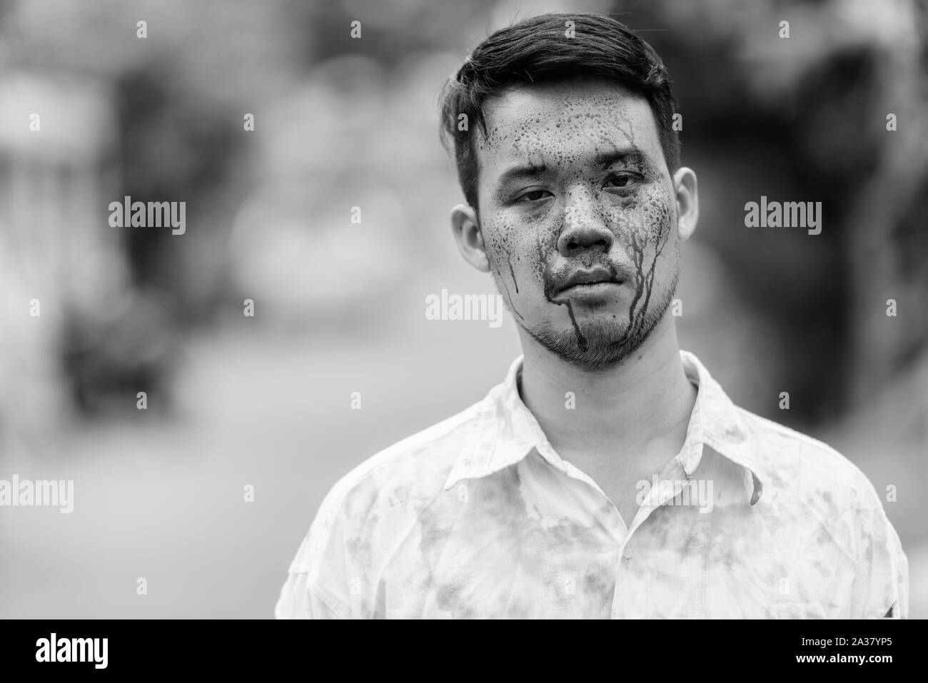 Young crazy Asian man with blood on face outdoors Stock Photo