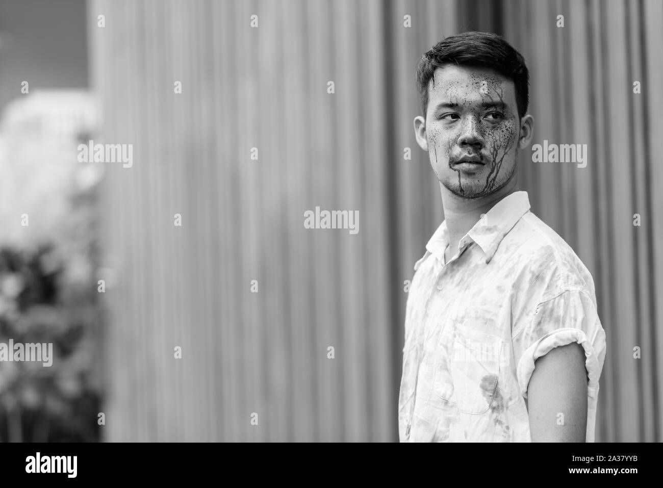 Young crazy Asian man thinking and looking at distance with blood on face outdoors Stock Photo
