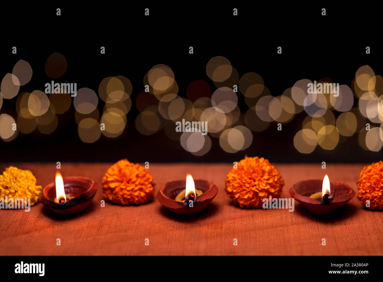 Diwali diya or clay oil lamp burning or glowing on a wooden surface decorated with marigold flowers and bokeh in background and copy space. Concept fo Stock Photo