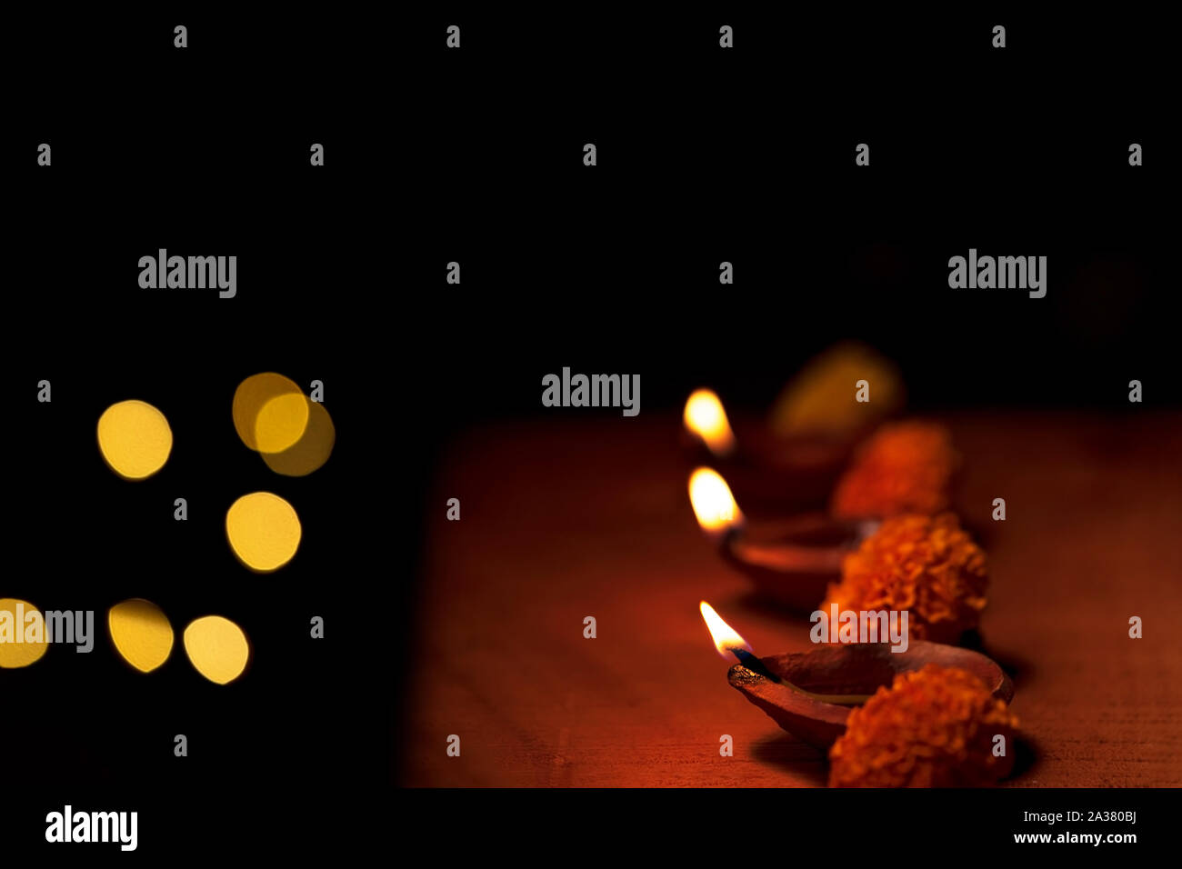 Diwali diya or terracotta oil lamps decorated in a row or line with flowers and copy space isolated in black background and bokeh lights. Concept for Stock Photo