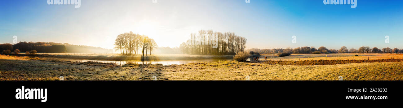Beautiful panorama of an autumn landscape at sunrise with river, forest and horses on a meadow Stock Photo