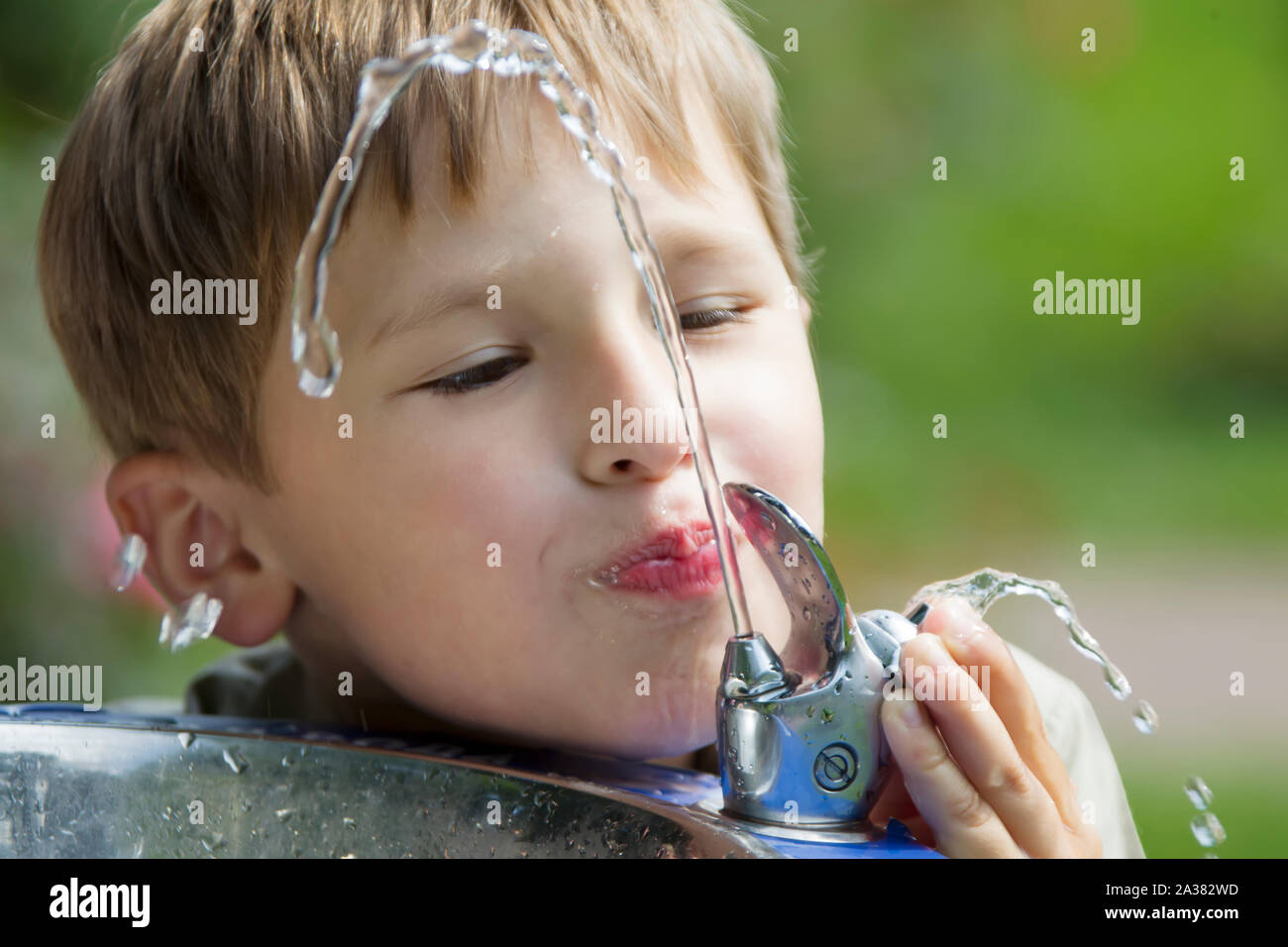 A child drinks water from a fountain. A jet of water and a drinking man