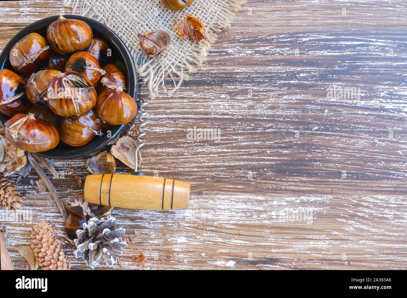 Tasty roasted chestnuts on ceramic bow, vintage corkscrew and natural cones on wooden rustic table. Festive winter holiday treats background. Top view Stock Photo