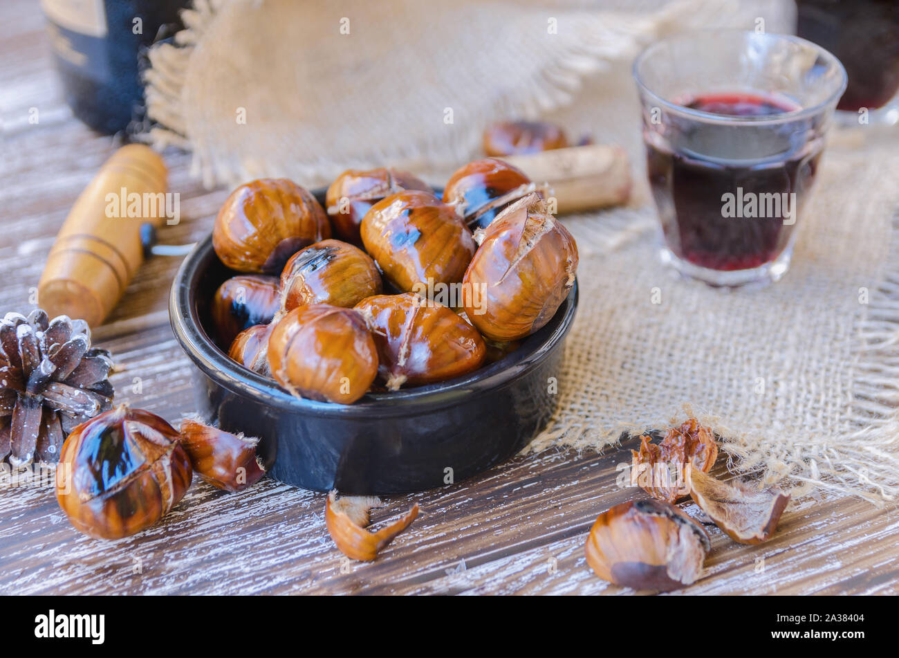 Tasty roasted chestnuts on ceramic bowl served with red wine on wooden rustic table. Festive winter holiday treats background. Stock Photo