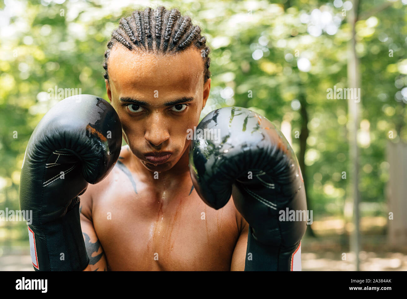 Sweated male boxer with mouth guard looking at camera while standing on sports ground outdoors Stock Photo