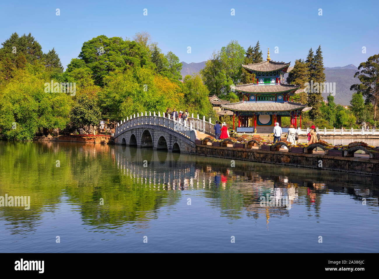 Lijiang, China - April 27, 2019: Tourists over the Suocui bridge with Moon Embracing Pavilion on the background. Stock Photo