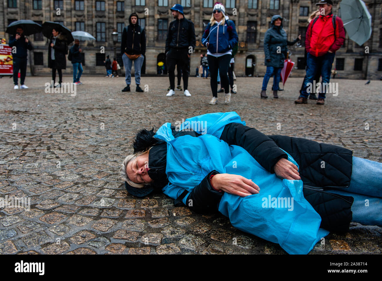 A woman lays on the ground during the performance.Before the International Extinction Rebellion week starts in Amsterdam, a group of XR activists gathered in the center of the city to make a People’s Declaration of Climate Crisis. They also performed a 'die-in-action' which involves a group of people assembling at a place and dropping dead on the ground while dressed up thematically and holding adequate posters and banners. Stock Photo