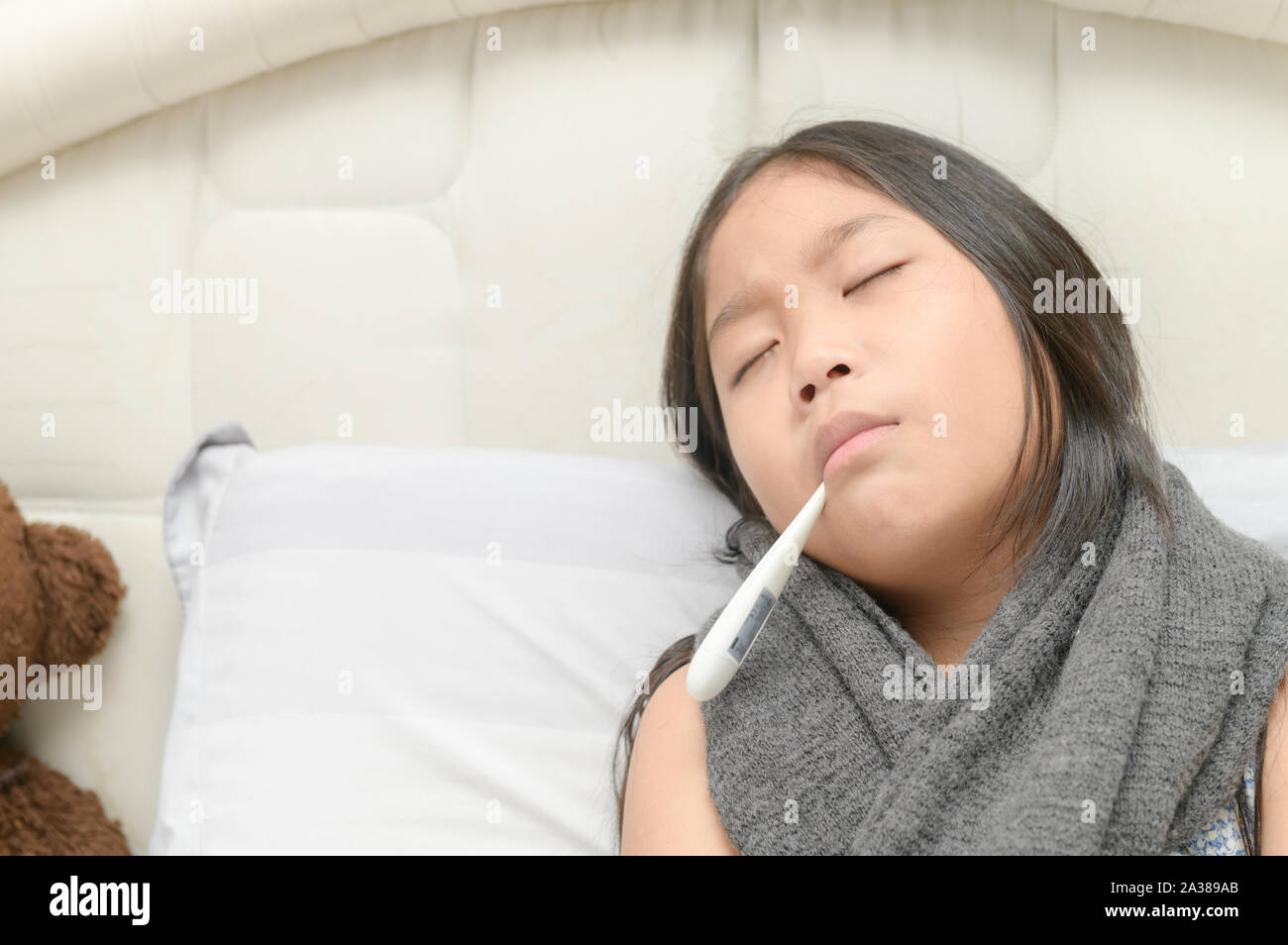 Sick girl with thermometer in mouth sitting on bed, Health care concept