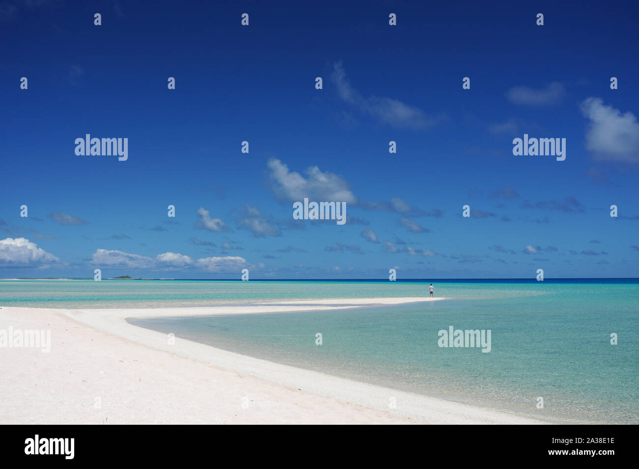 A man stands at the tip of a white sandy beach surrounded by a turquoise lagoon on the island of Fakarava, French Polynesia in the South Pacific Stock Photo