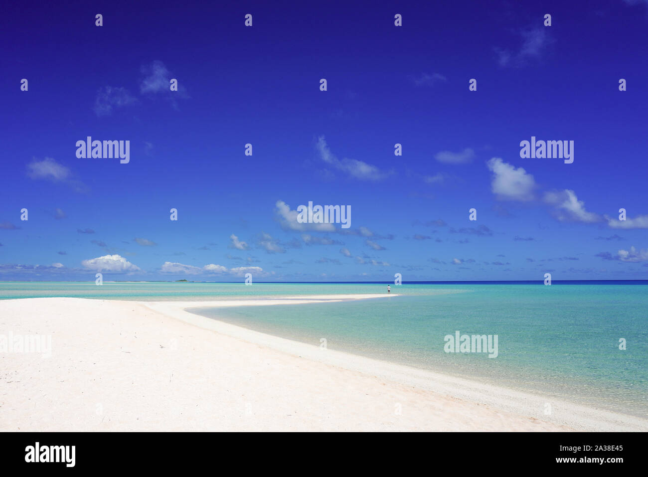 A man looks out over a tropical turquoise lagoon from a white sandy beach under a blue sky with copy space Stock Photo