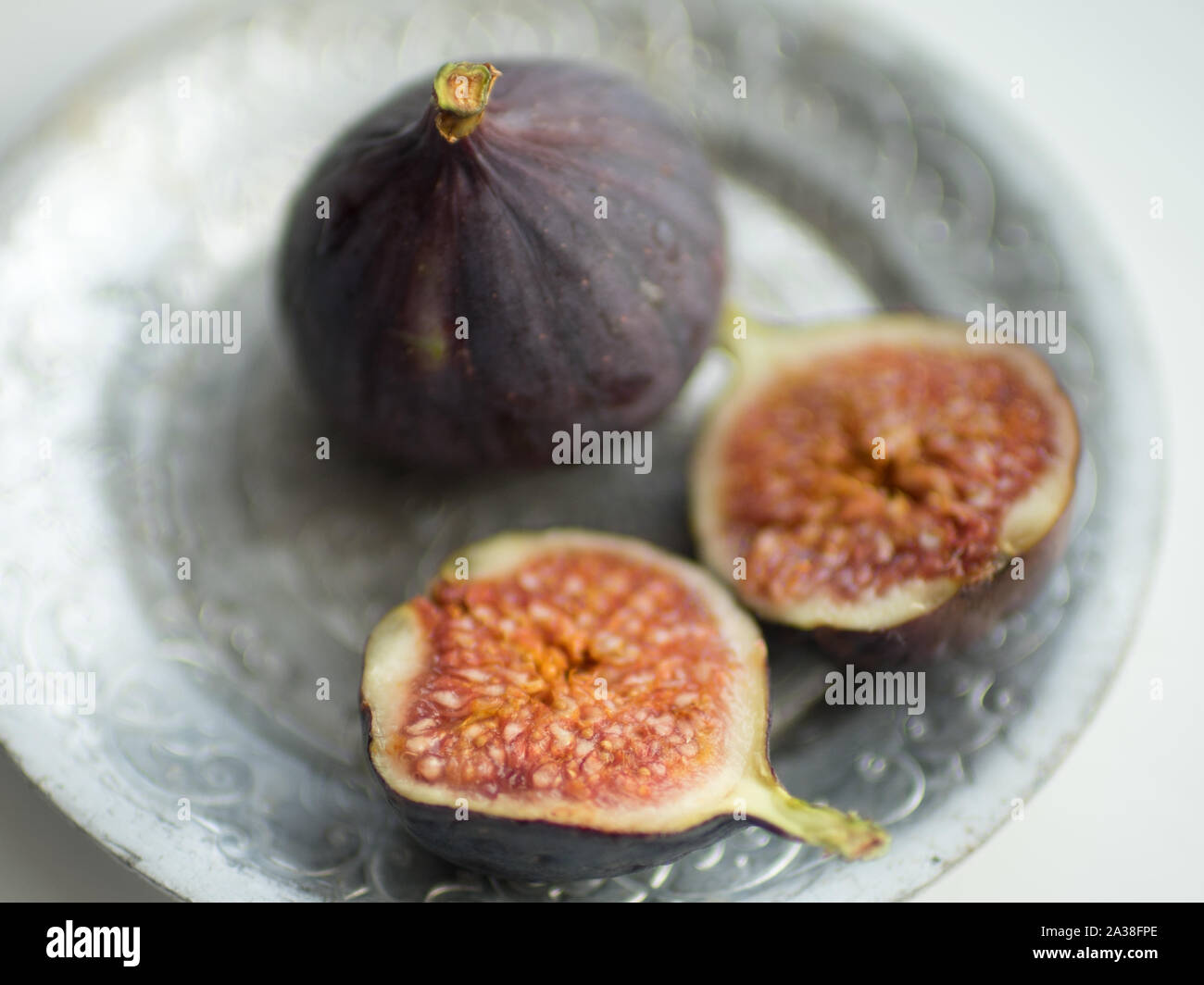 One whole fig and the second cut in half on a white table. Selective focus, closeup. Stock Photo
