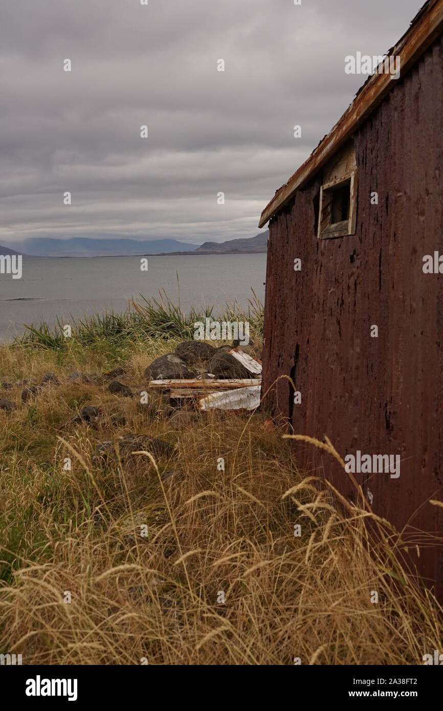 Mountains beyond the sea with an old  run down wooden hut in the foreground Stock Photo