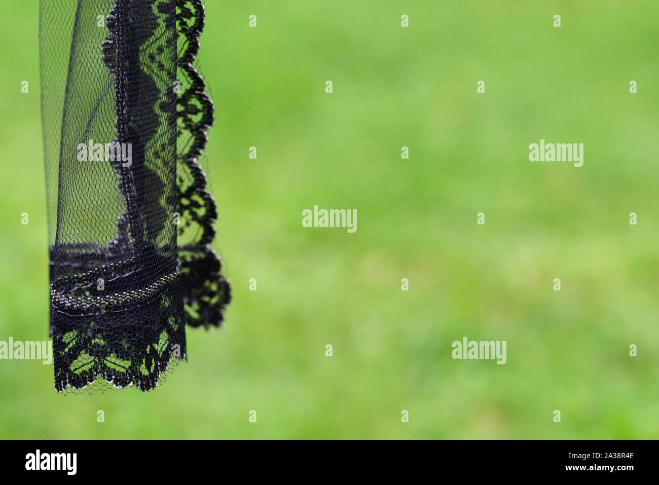 Part of a black mourning hanger hangs sideways against green meadow with background and space for text at the cemetery Stock Photo