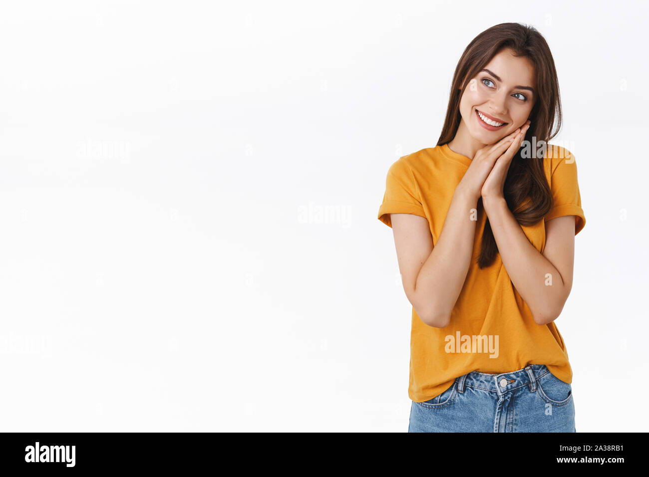 Cheerful, silly and dreamy romantic woman in yellow t-shirt, leaning face on palms and looking sideways with pleased, thoughtful expression, smiling Stock Photo