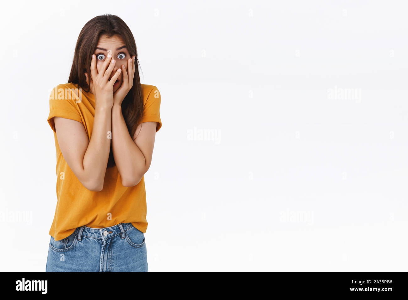 Scared, insecure timid young brunette girl, hiding face behind hands, peeking through fingers frightened, shivering from fear, watching horror movie Stock Photo