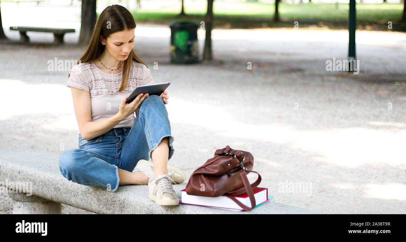 Girl with tablet sitting on a park bench Stock Photo - Alamy