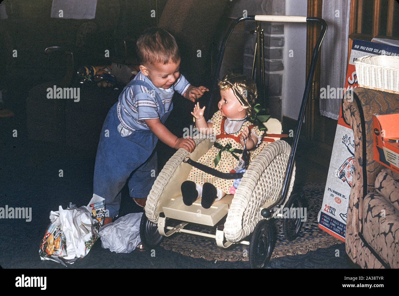 Toddler Plays with His Sister's Baby Carriage with Doll Christmas Present, 1953 Stock Photo