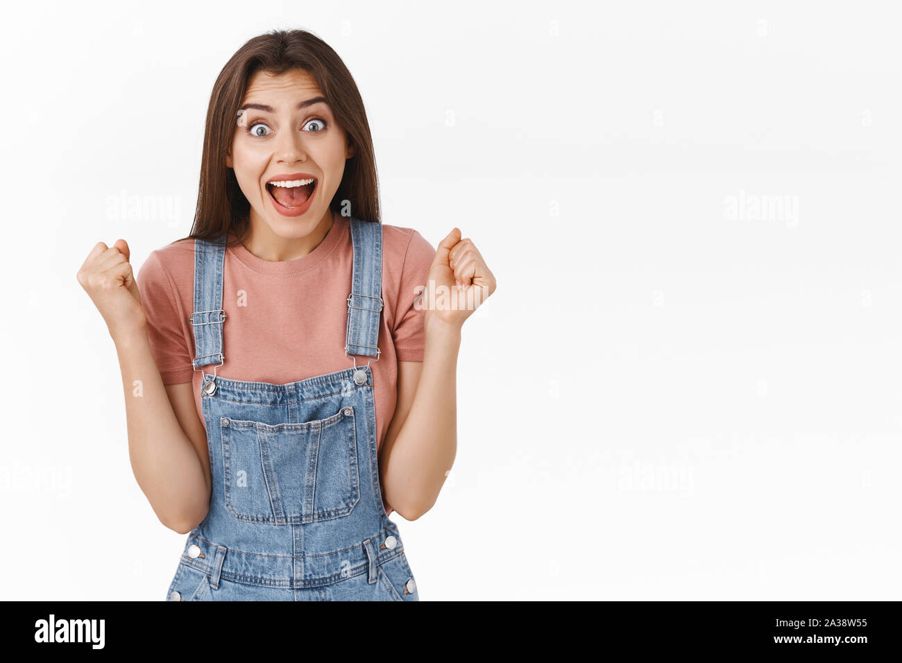 Cheerful, relieved attractive girl in overalls, lift hands up in cheer and happiness, screaming in rejoice, triumphing receive amazing good news Stock Photo