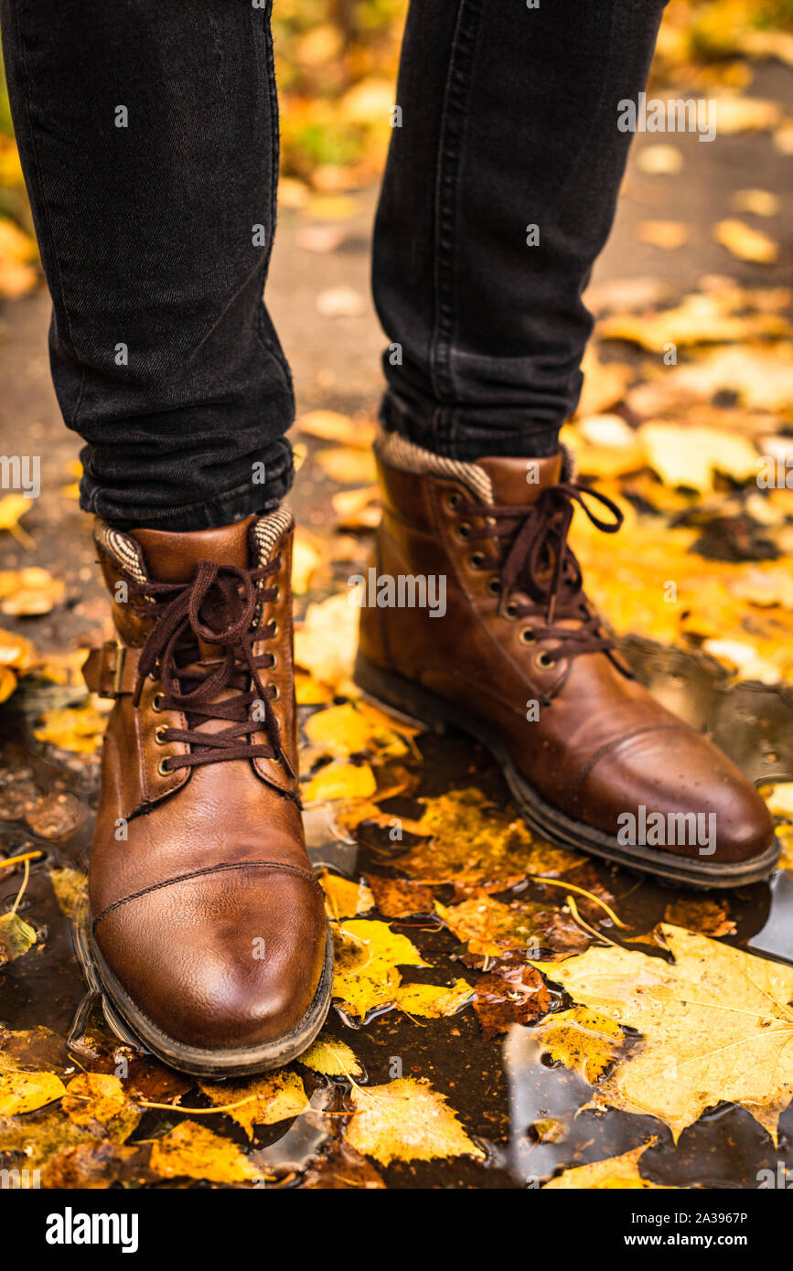 Man in brown leather boots standing in the puddle with autumn maple leaves. Conceptual trendy fall season image, hipster walking in the park Stock Photo