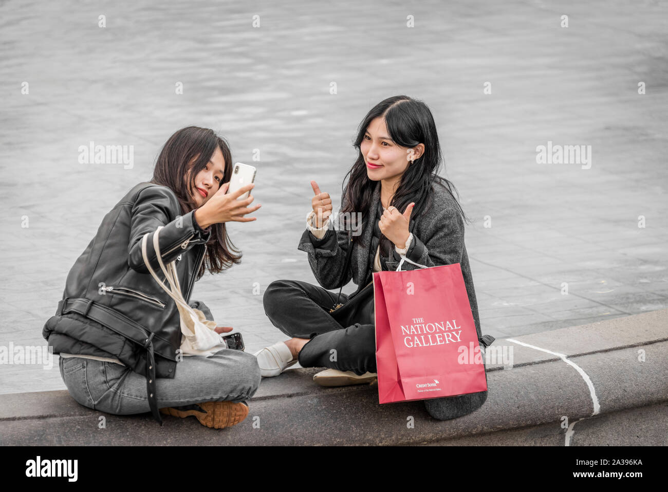 Two young girls pose for a 'selfie' on the edge of a fountain in Trafalgar Square, central London. Stock Photo