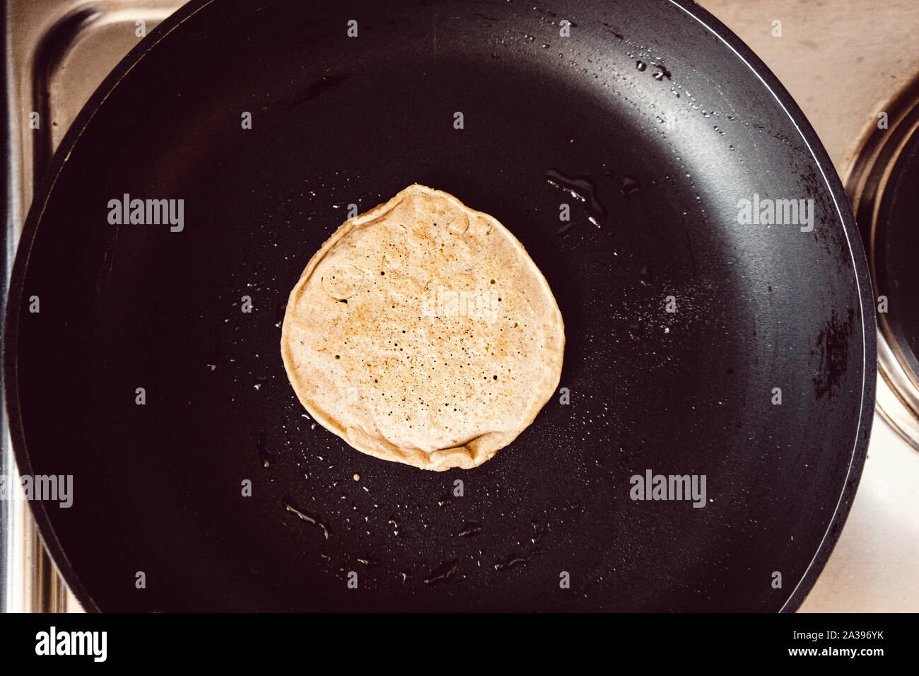Pancake cooking in a black pan in a kitchen Stock Photo