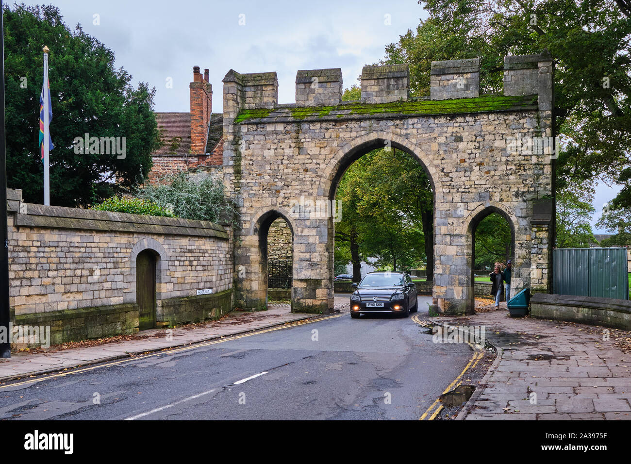 Priory Arch Gate near the cathedral in Lincoln, Lincolnshire with a black VW Passat driving through it and pedestrian to the side Stock Photo