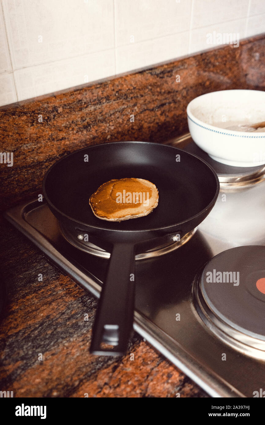 Pancake cooking in a black pan in a kitchen Stock Photo